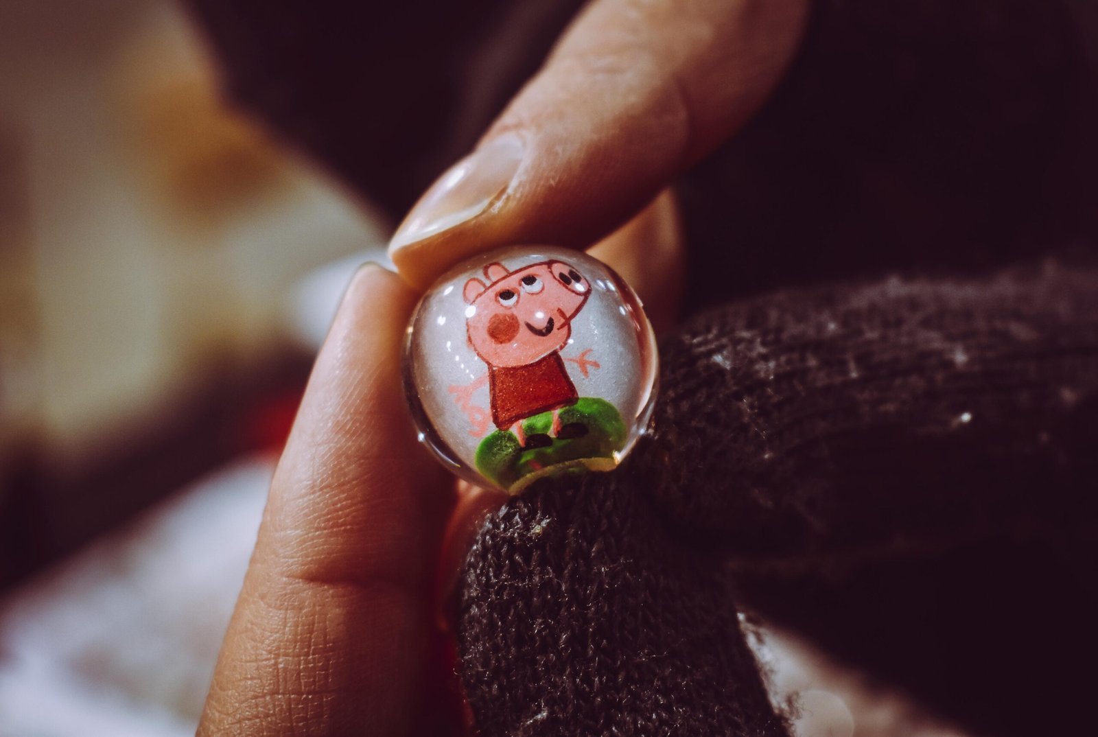 A close-up shot of a hand holding a glass marble featuring a cartoon character design.